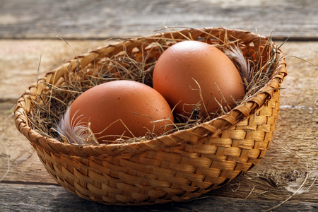 Two fresh farm chicken eggs in a rustic basket on a wooden table. Close-up shot.の写真素材