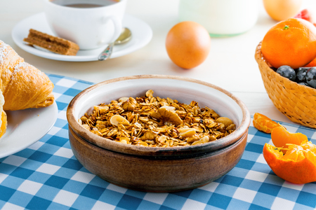Healthy food for breakfast on a white wooden table. Oatmeal granola with nuts, coffee, croissants, eggs, milk and fruits for delicious healthy meal. Close-up shot.の写真素材