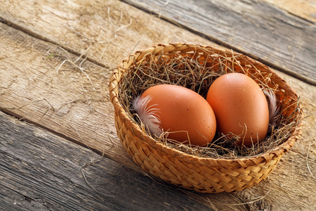 Two fresh farm chicken eggs in a rustic basket on a wooden table. Close-up shot. Top view.の写真素材