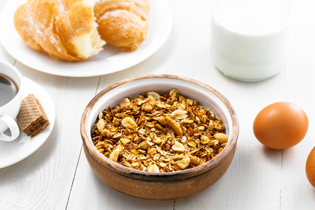 Oatmeal muesli with nuts, croissants, fruits, milk and coffee for delicious breakfast. Traditional healthy meal for breakfast on a table. Top view.の写真素材