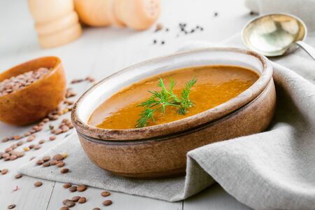 Delicious soup made of lentils in a rustic clay bowl served on a canvas tablecloth. Healthy vegetarian meal on a table. Close-up shot.の写真素材