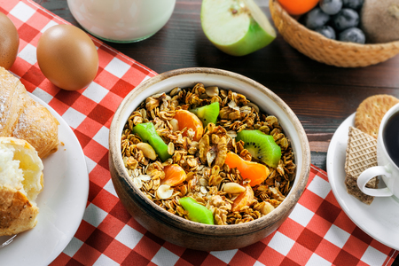 Oatmeal muesli with nuts, croissants, eggs, fruits, milk and coffee for delicious breakfast. Traditional healthy meal for breakfast on a brown table. Top view.の写真素材