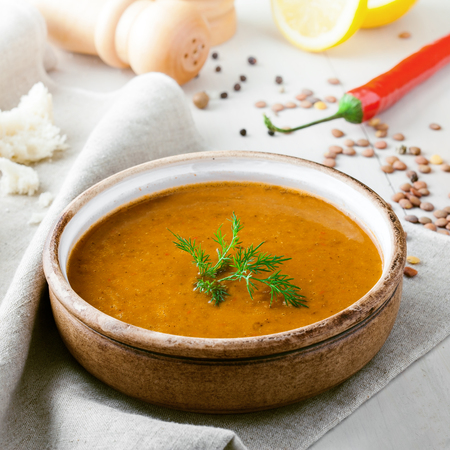 Delicious soup made of lentils in a rustic clay bowl served on a canvas tablecloth. Healthy vegetarian meal with bread, lemon and chili pepper on a table.の写真素材