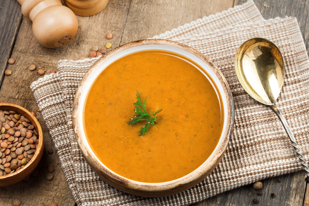 Soup made of lentil and vegetables in a rustic bowl on a canvas tablecloth. Delicious healthy vegetarian food on an old wooden table. Top view.の写真素材