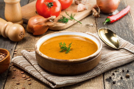 Healthy vegetarian lentil soup in a rustic clay bowl on an old wooden table. Delicious healthy meal served on a canvas tablecloth. Close-up shot.の写真素材