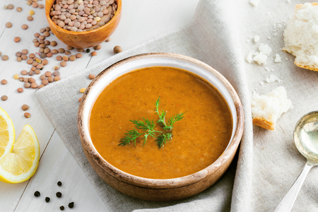 Delicious soup made of lentils in a rustic clay bowl served on a canvas tablecloth. Healthy vegetarian meal on a table. Top view shot.の写真素材