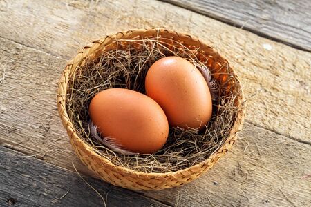 Couple of fresh chicken eggs in a rural basket with hey and feather on a wooden background. Close-up shot. Top view.の写真素材