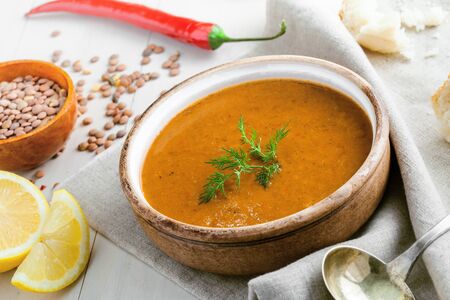 Soup made of lentil and vegetables in a rustic bowl with piece of bread on a canvas tablecloth. Delicious healthy vegetarian food on a white wooden table.の写真素材