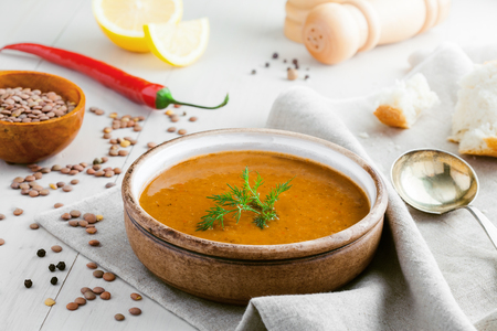 Bowl of delicious lentil soup with bread, lemon slice and spoon on a white wooden table. Traditional healthy vegetarian food.の写真素材