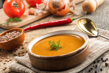 Delicious soup made of lentils in a rustic clay bowl served on a canvas tablecloth. Healthy vegetarian meal on a wooden table.の写真素材