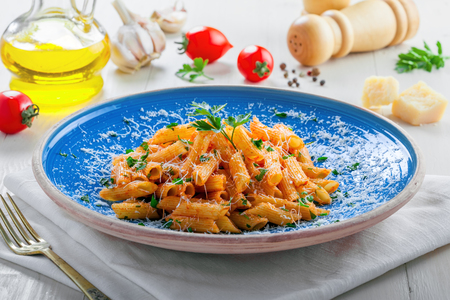 Traditional Italian meal made of penne pasta and arrabiata sauce with parsley on a white table. Delicious healthy Mediterranean food on a blue rustic plate.の写真素材