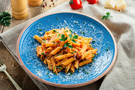 Traditional penne pasta with hot arrabiata tomato sauce and parsley on a rustic wooden table. Traditional Italian healthy food on a blue plate. Top view.の写真素材