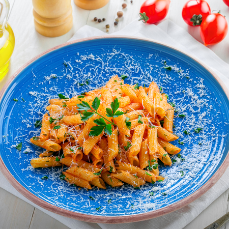 Italian penne pasta with arrabiata tomato sauce and parsley on a blue rustic plate. Traditional Italian healthy cuisine. Top view.の写真素材