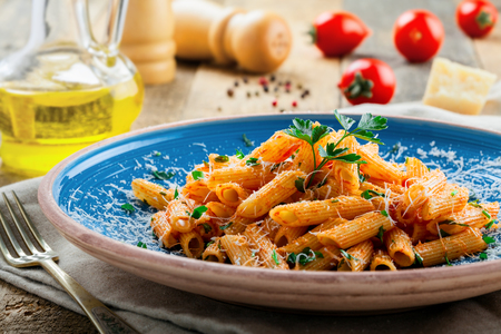 Tasty Italian penne pasta with tomato sauce on a blue plate. Delicious healthy Italian food on a rustic wooden table. Close-up shot.の写真素材