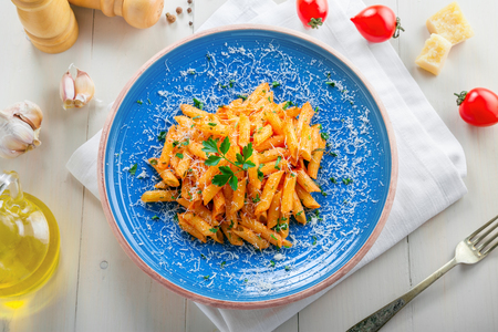 Traditional Italian penne pasta with arrabiata tomato sauce on a blue rustic plate. Delicious healthy Mediterranean cuisine food. Top view.の写真素材