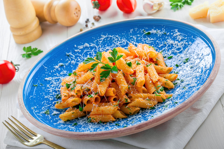 Traditional Italian meal made of penne pasta and arrabiata sauce with parsley on a white table. Delicious healthy Mediterranean food on a blue rustic plate.の写真素材