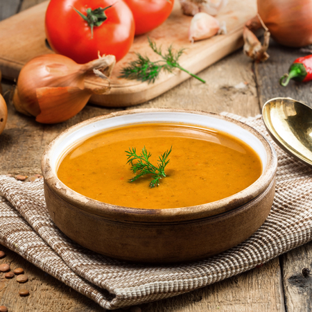 Healthy vegetarian lentil soup in a rustic clay bowl on an old wooden table. Delicious healthy meal served on a canvas tablecloth. Close-up shot.の写真素材