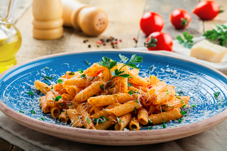 Italian penne pasta with arrabiata tomato sauce and parsley on a blue rustic plate. Traditional Italian healthy cuisine. Close-up shot.の写真素材