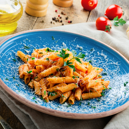 Traditional penne pasta with hot arrabiata tomato sauce and parsley on a rustic wooden table. Traditional Italian healthy food on a blue plate. Top view.の写真素材