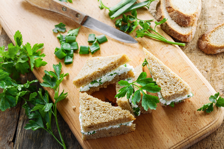 Healthy simple snack made of rye bread, cream cheese, fresh parsley and green onion on a table. Delicious small sandwiches. Top view.の写真素材