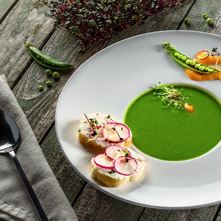 Pea cream soup in a rim soup plate. Classic European food on a rustic wooden table.の写真素材
