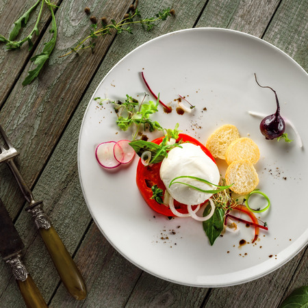 Delicious Italian caprese on a rustic wooden table. Healthy salad made of mozzarella cheese, tomatoes and herbs on a plate. Top view.の写真素材