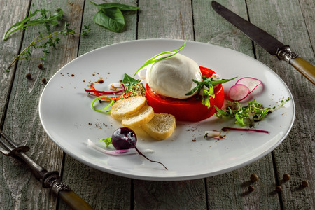 Classic Italian cuisine meal made of mozzarella, tomato and herbs on a table. Caprese salad on a white round plate.の写真素材