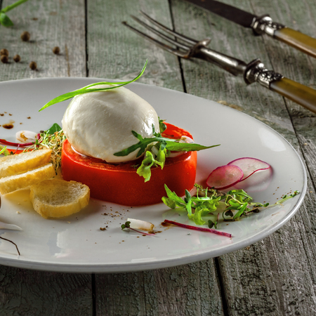 Italian classic caprese salad on a white round plate. Delicious healthy meal made of mozzarella and tomato on a table.の写真素材