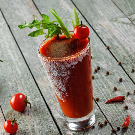 Glass of bloody mary on a wooden table. Delicious alcohol cocktail made of tomato juice, vodka, pepper, salt, lemon juice, celery and other flavorings.の写真素材