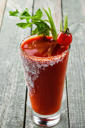 Glass of bloody mary on a wooden table. Delicious alcohol cocktail made of tomato juice, vodka, pepper, salt, lemon juice, celery and other flavorings. Close-up shot.の写真素材