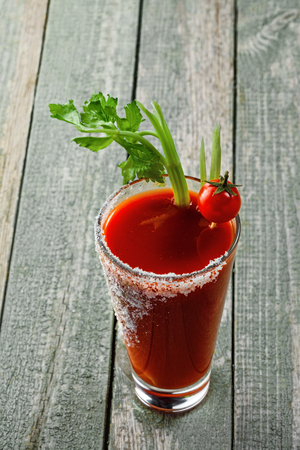 Glass of classic bloody mary cocktail on a rustic wooden table. Delicious alcoholic drink made of tomato juice, vodka, pepper, salt, lemon juice, celery and other flavorings.の写真素材