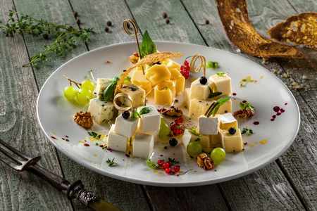 Delicious cheese platter with grape, fruits, basil and other appetizers on a rustic wooden table. Set of parmesan, gouda, gorgonzola, brie, camembert and other cheeses on a plate.の写真素材