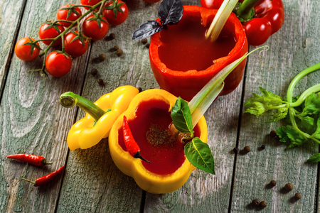 Bloody mary in yellow and red sweet bell peppers on a wooden table. Delicious alcohol cocktail made of tomato juice, vodka, pepper, salt, lemon juice, celery and other flavorings.Top view, right above shot.の写真素材