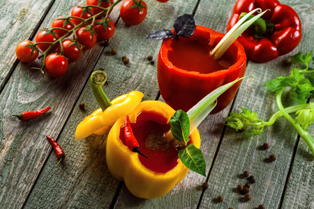 Bloody mary cocktail in yellow and red sweet bell peppers on a rustic wooden table. Delicious alcoholic drink made of tomato juice, vodka, pepper, salt, lemon juice, celery and other flavorings. Top view shot.の写真素材