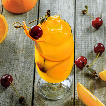Fruit punch cocktail made of vodka, fruit juice, orange and cherry on a wooden table. Alcoholic drink in a long hurricane glass.の写真素材