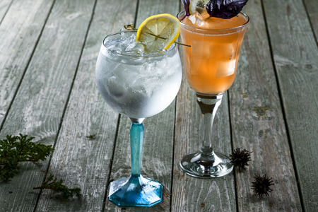 Alcoholic gin and tonic cocktail with drink made of rum, soda, ice and basil leaf in a long glass on a wooden table.の写真素材