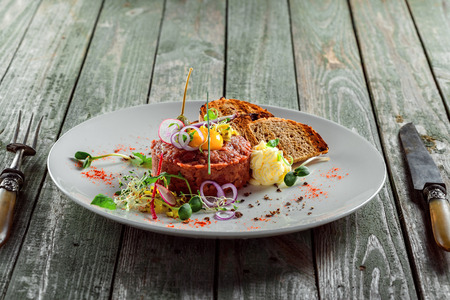 Delicious tartare with toasted bread and salad on a plate. Healthy lunch meal made of raw meat. Classical French cuisine.の写真素材