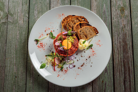 Plate with delicious tartare, toasted bread and salad on a wooden table. Healthy gourmet French food made of raw meat. Top view.の写真素材