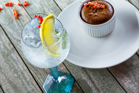 Gin and tonic cocktail with sweet chocolate mousse a wooden table. Alcoholic drinks in a glass with dessert.の写真素材