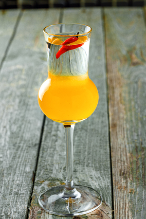 Delicious alcoholic shot drink made of peach liqueur, lemon fresh and tequila on a wooden table. Classic cocktail shot.の写真素材