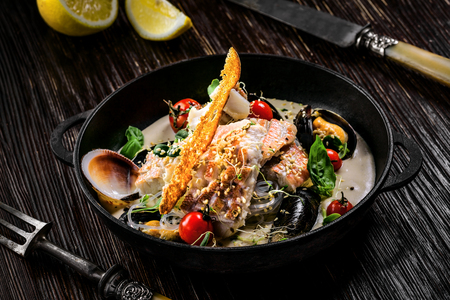 Delicious Asian meal made of sea bass fish, mussels, crab meat and other seafood with tomato and rice noodles on a rustic wooden table.の写真素材