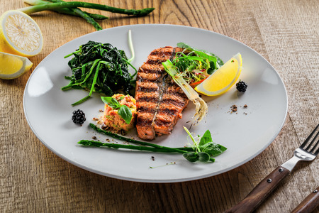 Grilled salmon fish steak with vegetable salad on a plate. Gourmet seafood meal made of fish and vegetables. Healthy food on a table.の写真素材