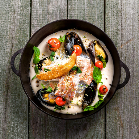Sea bass fish fillet with mussels, crab meat and cockles with vegetables, cream sauce and rice noodles. Healthy Asian seafood meal on a table. Top view.の写真素材