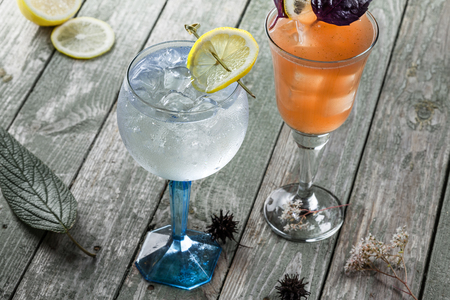 Delicious gin and tonic cocktail with drink made of rum, soda, ice and basil leaf on a wooden table. Alcoholic drinks in a glass.の写真素材