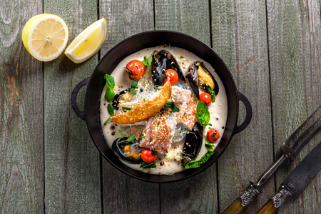 Delicious Asian meal made of sea bass fish, mussels, crab meat and other seafood with tomato and rice noodles on a rustic wooden table. Top view.の写真素材
