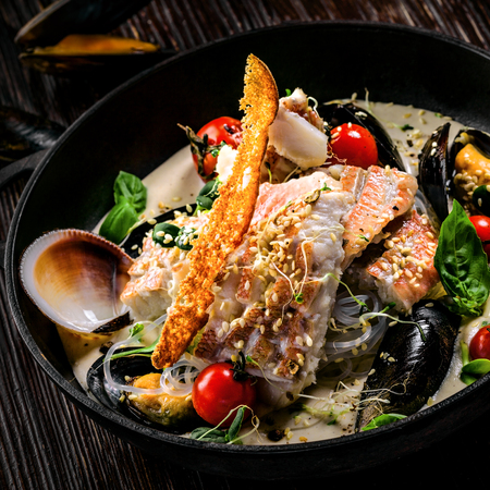 Gourmet Asian meal mad of seafood such as sea bass fish, mussels, crab meat and cockles with vegetables and rice noodles on a table.の写真素材
