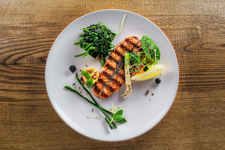 Salmon fish stake cooked on a grill with healthy salad on a plate. Healthy food made of fish and vegetables on a table. Top view.の写真素材