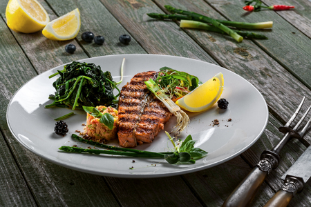 Gourmet grilled salmon fish steak and vegetable salad on a plate. Delicious healthy meal made of fish and vegetables on a rustic table.の写真素材