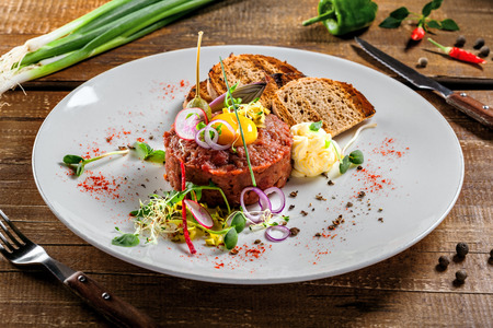 Plate with delicious tartare, toasted bread and salad on a wooden table. Healthy gourmet French food made of raw meat.の写真素材