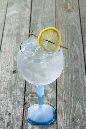 Glass gin and tonic cocktail with lemon slice on a wooden table.の写真素材